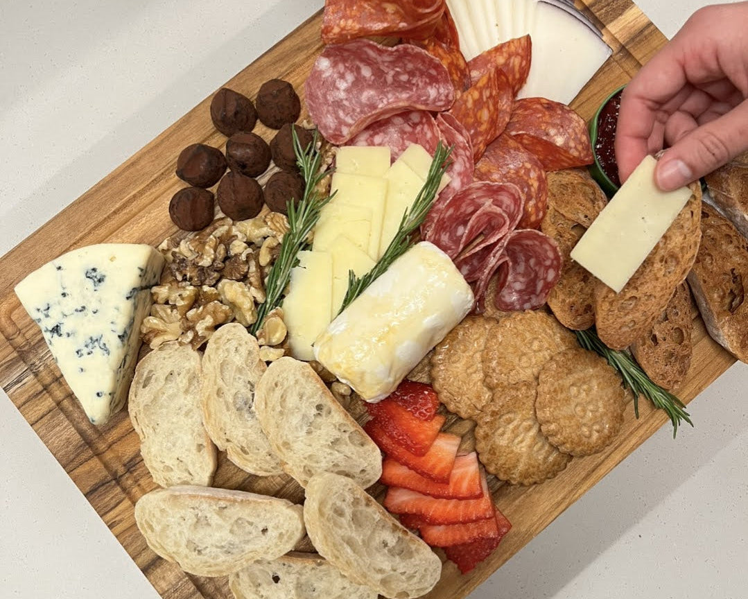 Wooden cutting board with assorted meats, cheeses, and bread on a white surface.